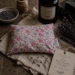 Load image into Gallery viewer, Floral-patterned heat pillow with lavender and bottle on wooden surface
