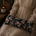Load image into Gallery viewer, Floral lupin heat pillow on a bed next to a person wearing a sweater, with a candle in the background.
