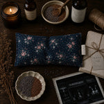 Load image into Gallery viewer, Decorative items including a floral eye pillow, bowls with seeds, a candle, and a book on a wooden surface.

