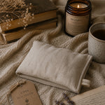 Load image into Gallery viewer, Heated pillow on a textured surface with books, a candle, and a mug.
