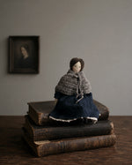 Load image into Gallery viewer, Heirloom doll sitting on vintage books with a blurred portrait in the background - handmade by Artist Kate Karsten
