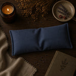 Load image into Gallery viewer, Blue eye pillow on a wooden surface with a candle and dried flowers.
