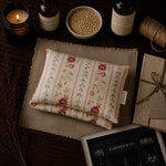 Load image into Gallery viewer, Folded floral fabric on a textured surface with candles and bottles in the background
