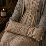 Load image into Gallery viewer, Person holding a floral-patterned neck lupin heat pillow with a candle and plant in the background
