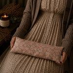 Load image into Gallery viewer, Person holding a floral-patterned lupin heat pillow with a candle and dried plants in the background
