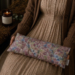 Load image into Gallery viewer, Person holding a floral fabric lupin heat pillow with a candle and plant in the background

