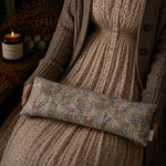 Load image into Gallery viewer, Person holding a floral-patterned lupin heat pillow with a candle and decorative elements in the background
