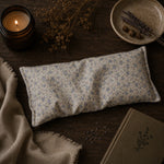 Load image into Gallery viewer, Floral-patterned eye pillow on a wooden surface with a candle and dried elements.
