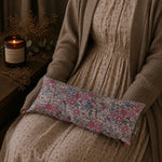 Load image into Gallery viewer, Person wearing a brown sweater with a floral fabric lupin heat pillow on a couch, next to a lit candle and dried plants.
