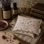 Load image into Gallery viewer, Floral heat pillow on a wooden surface with dried lavender, books, and bottles.

