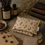 Load image into Gallery viewer, Folded fabric heat pillow with floral pattern on a wooden surface with herbs and books.
