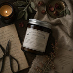 Load image into Gallery viewer, Jar of Chandler Parfumerie Karsten &amp; Co. candle with a lit candle, scissors, and dried plants on a textured surface.
