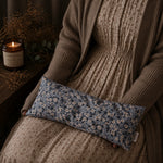 Load image into Gallery viewer, Person wearing a brown sweater holding a blue floral lupin heat pillow with a candle and dried plants in the background.
