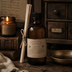 Load image into Gallery viewer, Bottle of parfum with a label, candles, and reeds on a wooden surface.
