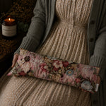 Load image into Gallery viewer, Person holding a floral fabric lupin heat pillow with a candle and decorative elements in the background
