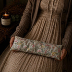 Load image into Gallery viewer, Person holding a floral fabric lupin heat pillow with a candle and decorative elements in the background
