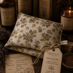 Load image into Gallery viewer, Floral-patterned heat pillow with a tag on a background of books and lavender items.
