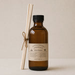 Load image into Gallery viewer, Brown bottle reed diffuser with black cap and label, accompanied by white sticks on a beige background
