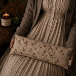 Load image into Gallery viewer, Person holding a floral-patterned lupin heat pillow with a candle and plant in the background
