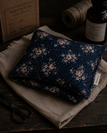 Load image into Gallery viewer, Floral-patterned heat pillow on a textured surface with a bottle and paper in the background
