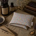 Load image into Gallery viewer, Floral-patterned heat pillow on a wooden surface with herbs and books in the background
