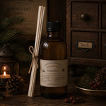 Load image into Gallery viewer, Reed diffuser Bottle of Chandler Parfum with 'Christmas' label, surrounded by candles and pine cones on a wooden surface.
