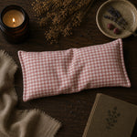 Load image into Gallery viewer, Red and white checkered eye pillow on a wooden surface with a candle and dried flowers.
