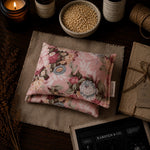 Load image into Gallery viewer, Floral-patterned heat pillow on a textured surface with candles and books in the background
