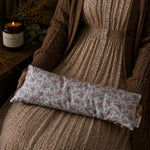 Load image into Gallery viewer, Person holding a floral-patterned lupin heat pillow with a candle and plant in the background
