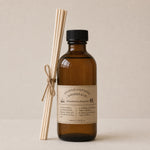 Load image into Gallery viewer, Brown bottle reed diffuser with label and wooden sticks on a beige background
