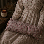Load image into Gallery viewer, Person wearing a floral-patterned garment with a matching lupin heat 
pillow, next to a lit candle on a wooden surface.
